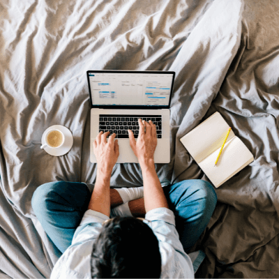 Overhead view of a man working on a laptop from his bed at home